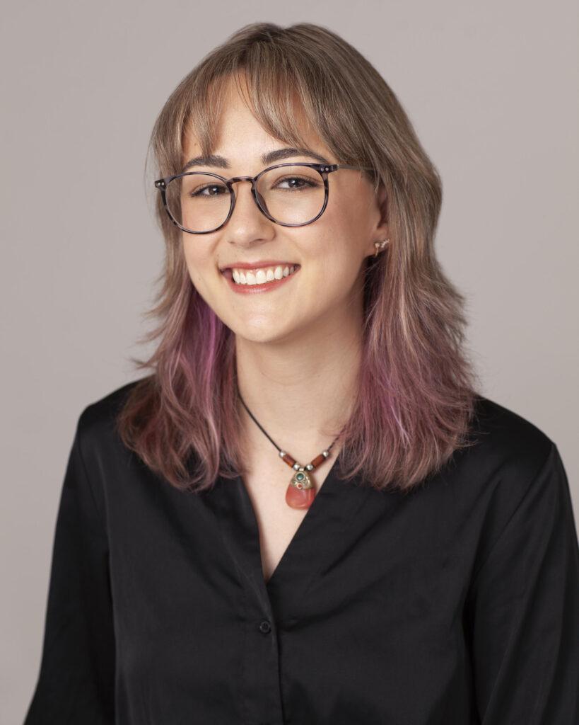 Paula Carrizosa, LMSW, smiling at the camera, wearing glasses, a necklace with a red charm, and a black shirt.